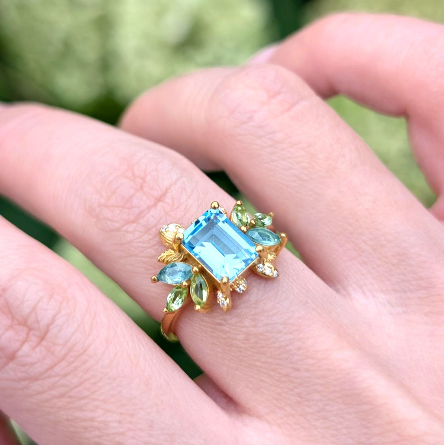 Verlobungsring mit blühendem Smaragdschliff, blauem Edelstein und blattförmigem Halo